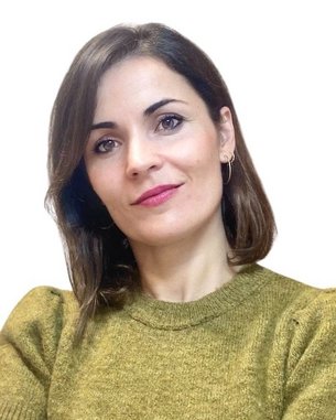 A woman with shoulder-length brown hair is wearing an olive green short-sleeved top and is looking directly at the camera.