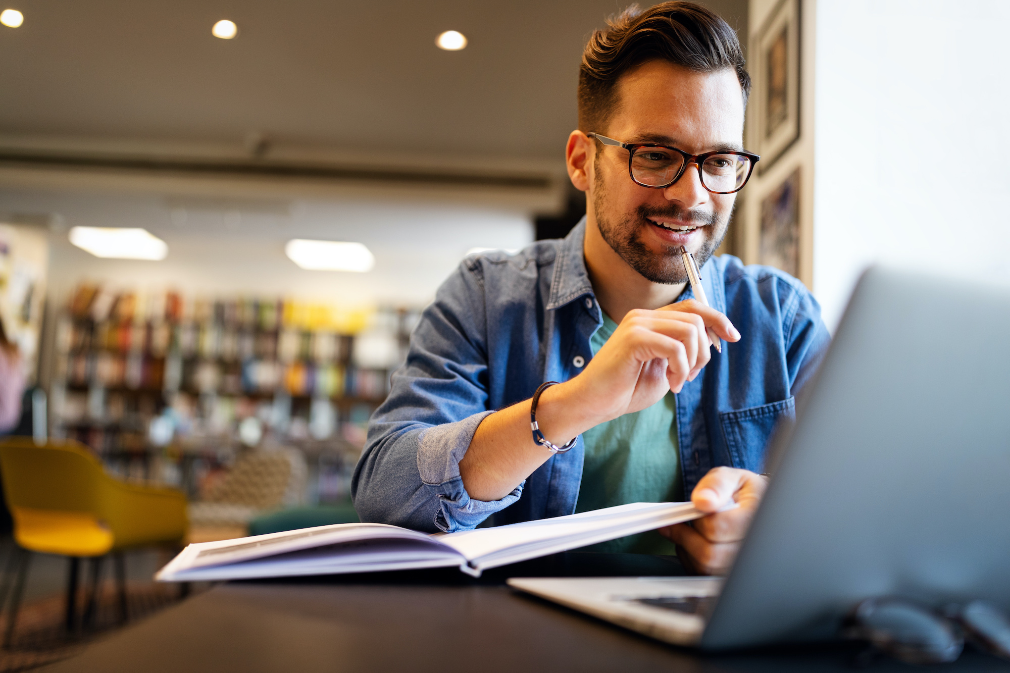 Student sitzt in Bibliothek und lacht in den Laptop