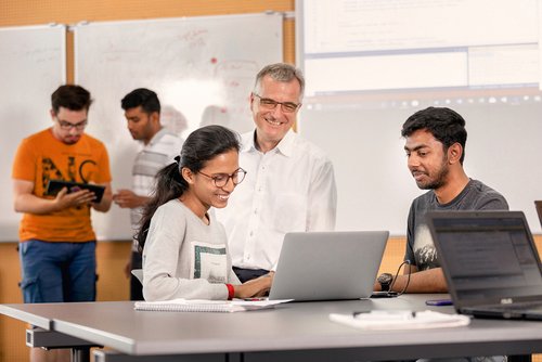 Studenten und Dozent schauen gemeinsam auf Laptop