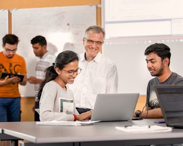 Studenten und Dozent schauen gemeinsam auf Laptop