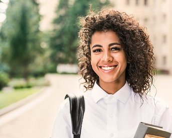 Studentin mit Locken hält Unterlagen in der Hand und lacht