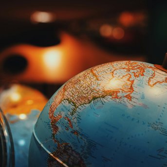 Ein Globus zeigt die Kontinente und Ozeane der Erde, mit einem Fokus auf Nordostasien. Der Globus ist teilweise transparent und steht in einer Umgebung mit unscharfen, farbigen Objekten im Hintergrund.