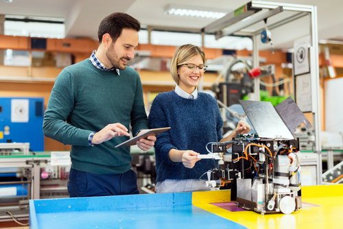 Two people in a lab are working on a technical device, with one holding a tablet and the other inspecting the device.