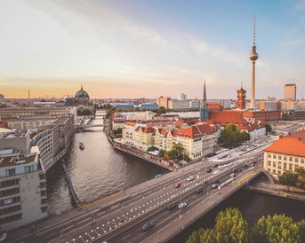 Blick auf die Berliner Skyline mit dem Fernsehturm, historischen Gebäuden und der Spree. Die Szene zeigt eine Mischung aus moderner und klassischer Architektur, umgeben von Wasser und Straßenverkehr.