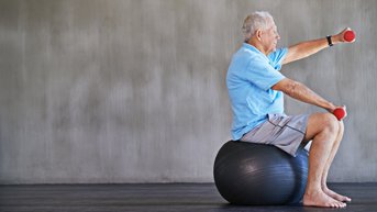 Patient sitzt auf einem Gymnastikball und macht Übungen mit Hanteln 