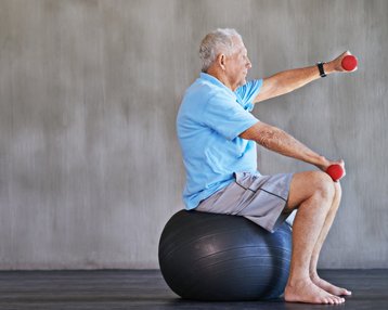 Patient sitzt auf einem Gymnastikball und macht Übungen mit Hanteln 