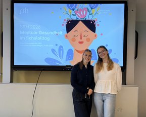 Zwei Frauen stehen vor einem Bildschirm, der Informationen über mentale Gesundheit im Schulalltag zeigt.