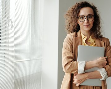 Studentin mit Locken und Mac-Rechner in der Hand. 