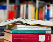 Portraitfoto von einem Stapel Bücher vor einem Bücherregal der Bibliothek