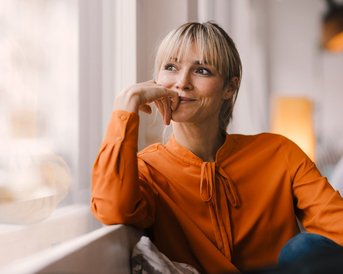 Frau mit orangener Bluse schaut aus dem Fenster