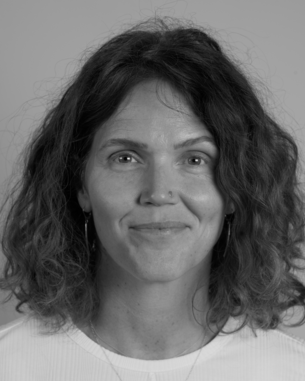 Portrait of a woman with curly, shoulder-length hair and earrings, smiling directly at the camera.