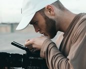 Ein Mann mit einer weißen Kappe betrachtet sorgfältig eine Kamera. Er hält die Kamera mit einer Hand und justiert sie mit der anderen. Der Fokus liegt auf seiner Konzentration und der professionellen Ausrüstung.