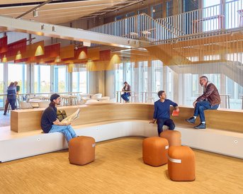 Modern interior design featuring seating areas, with several people relaxing or working, and large windows that let in natural light.