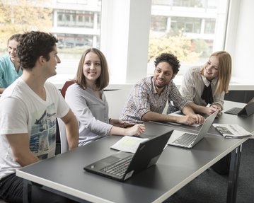 Vier Studierende unterhalten sich in einem Seminarraum. 