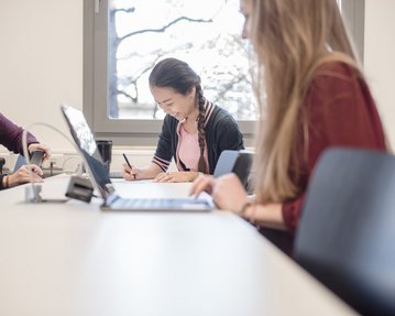 Zwei Studentinnen arbeiten am Tisch in der Uni mit Laptop. 