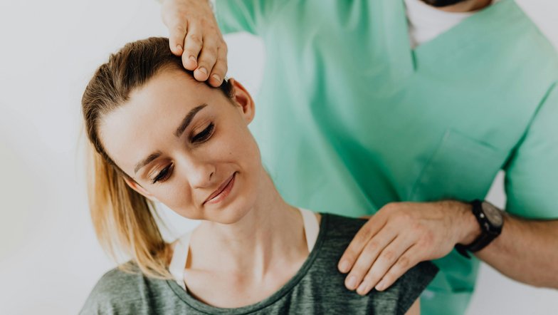 Kategorie Therapie studieren Studium SRH University A woman is receiving a neck massage from a male therapist. The therapist has his hand on her head while she looks relaxed. Both are wearing comfortable clothing.