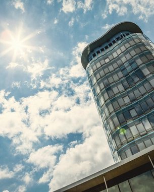 Ein modernes Hochhaus mit einer geschwungenen Fassade, das unter einem klaren Himmel mit Wolken und Sonnenschein steht.