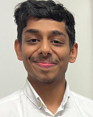 A young man with dark, curly hair and a slight smile is wearing a white shirt. The background is neutral and bright.