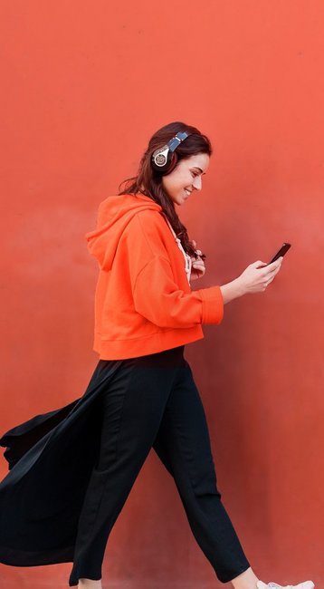 Studentin mit Handy in der Hand läuft an einer roten Wand vorbei