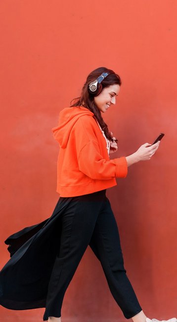 Studentin mit Handy in der Hand läuft an einer roten Wand vorbei