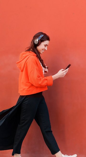 Studentin mit Handy in der Hand läuft an einer roten Wand vorbei