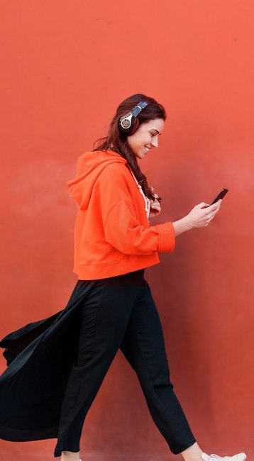 Studentin mit Handy in der Hand läuft an einer roten Wand vorbei