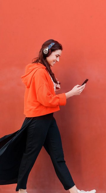 Studentin mit Handy in der Hand läuft an einer roten Wand vorbei