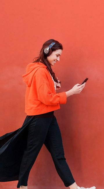 Studentin mit Handy in der Hand läuft an einer roten Wand vorbei