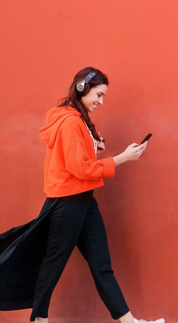 Studentin mit Handy in der Hand läuft an einer roten Wand vorbei