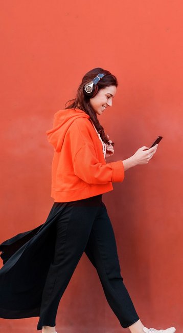 Studentin mit Handy in der Hand läuft an einer roten Wand vorbei