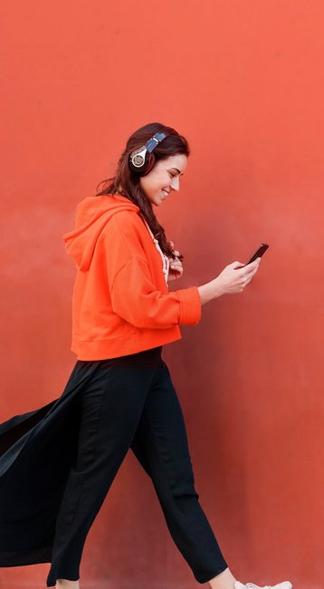 Studentin mit Handy in der Hand läuft an einer roten Wand vorbei