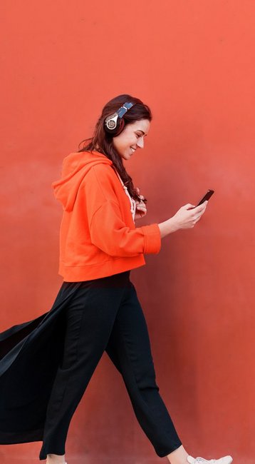 Studentin mit Handy in der Hand läuft an einer roten Wand vorbei