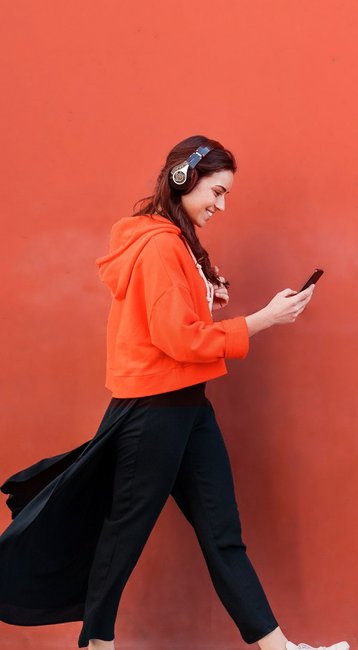 Studentin mit Handy in der Hand läuft an einer roten Wand vorbei