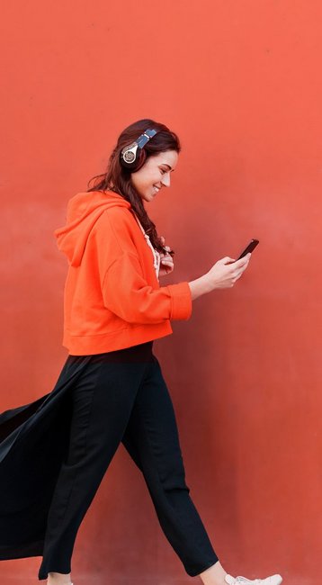 Studentin mit Handy in der Hand läuft an einer roten Wand vorbei