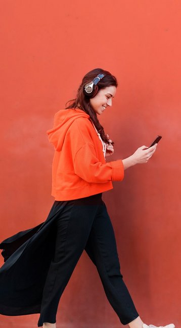 Studentin mit Handy in der Hand läuft an einer roten Wand vorbei