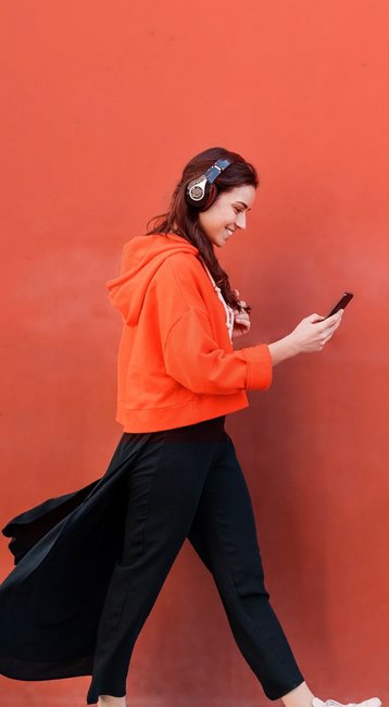 Studentin mit Handy in der Hand läuft an einer roten Wand vorbei