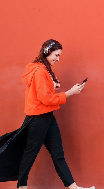 Studentin mit Handy in der Hand läuft an einer roten Wand vorbei