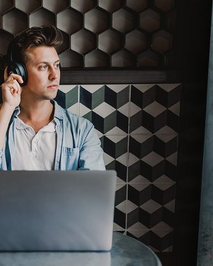 Student with headphones sitting at a table in a café, working on his laptop.