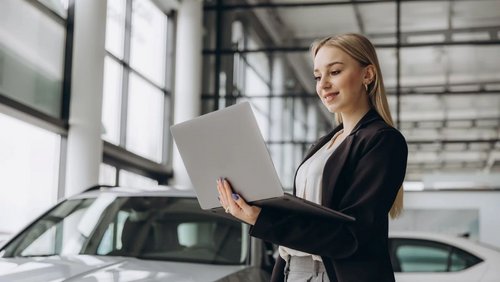 Woman in a car dealership holding a laptop.