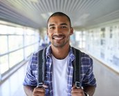 Student in a checkered shirt and backpack smiles at the camera.