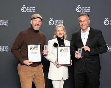 Drei Personen halten Auszeichnungen des German Design Awards 2023 in der Hand, stehen vor einem neutralen Hintergrund.