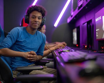 Ein junger Mann mit Kopfhörern sitzt an einem Computerarbeitsplatz in einem Gaming-Raum, bereit zum Spielen.