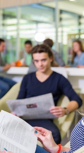 Studentin lächelt in die Kamera während sie ein Buch in der Hand hält